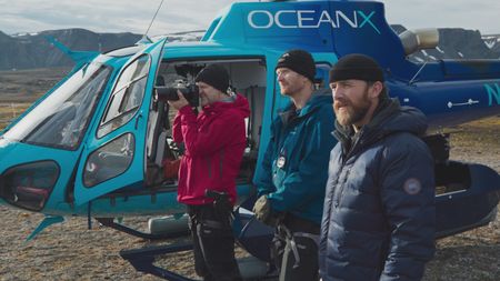 Jon Aars, Rolf-Arne Ølberg, and Aldo Kane stand next to one of the OceanXplorer's helicopters, taking photos and observing the recently collar tagged female polar bear and her cub to ensure their safety. (National Geographic)