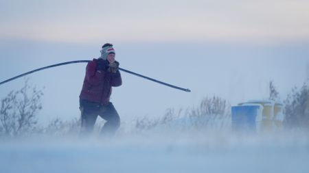 Sue Aikens carries a pipe over her shoulder during a severe winter storm so they donìt get buried under the drifts and freeze to the ground. (BBC Studios/Michael Cheeseman)