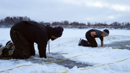 Chevie Roach teaches his son Ryder how to set a fish net under the ice. (BBC Studios/Brian Bitterfeld)