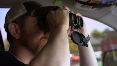 HSI Agent Connor uses binoculars to get a better view of a suspect during an operation in San Diego, Calif. (National Geographic)