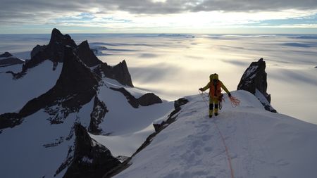 Professional alpinist Conrad Anker summits a mountain in Queen Maud Land, in Antarctica. He walks on top of the snow-capped mountain holding the ropes he used to climb.  (credit: National Geographic/Cedar Wright)