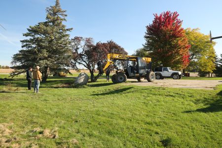 Charles Pol and Seth Doble watch as Ben Reinhold moves a large rock from the front of the property to the Pol family farm's new garden with a telehandler. (National Geographic)
