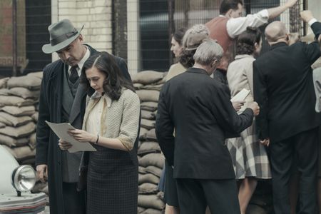 A SMALL LIGHT - Otto Frank, played by Liev Schreiber, and Miep Gies, played by Bel Powley, check a list of names at the Red Cross as seen in A SMALL LIGHT. (Credit: National Geographic for Disney/Dusan Martincek)