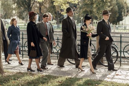 A SMALL LIGHT - Miep and Jan are accompanied by friends and family as they walk to the Civil Registry Office to get married, as seen in A SMALL LIGHT. (From left: Sally Messham as Bep, Cosima Shaw as Genofeva, Laurie Kynaston as Cas, Brian Caspe as Laurens, Liev Schreiber as Otto Frank, Bel Powley as Miep Gies, and Joe Cole as Jan Gies). (Credit: National Geographic for Disney/Dusan Martincek)
