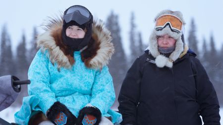 Carol Hailstone and her sister Tinmiaq wait by the sled that fell off their mother's snowmobile while traveling. (BBC Studios/Pedro Delbrey)