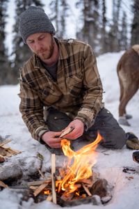 Johnny Rolfe adds kindling to a fire while he builds a box seat for his dog, Java. (BBC Studios Reality Production/Patrick Henderson)