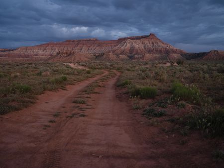 A dirt road leads towards sandstone mesa formations at dusk.  (National Geographic/Rick Smith)