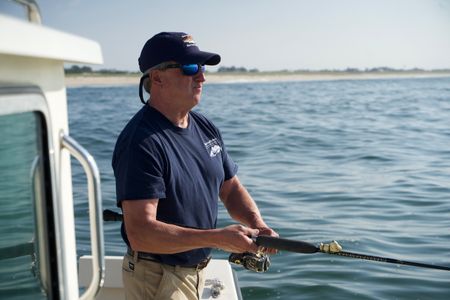 Dr. Greg Skomal, stands reeling in his rod, on a sunny day fishing for menhaden just of the shore of Long Island. (National Geographic/Brandon Sargeant)