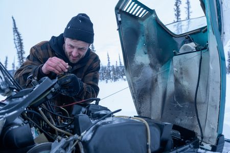 Johnny Rolfe fixes the carburetor on his snowmobile, and dethaws the frozen lines after it broke down in the wilderness. (BBC Studios Reality Productions/Tyler Colgan)