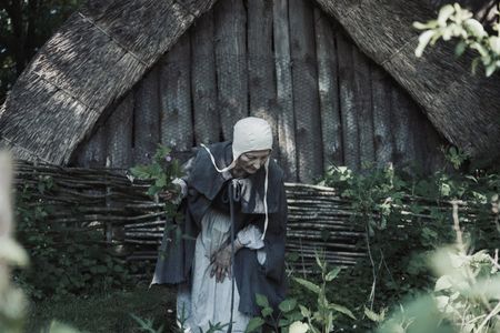 Agnes Sampson holds a bunch of medicinal plants and herbs in one hand as she searches for more in the field. (Dash Productions Services LTD/Antoan Ivanov)