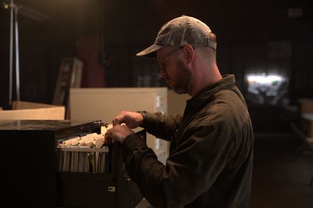 Journalist Dylan Taylor-Lehman is pictured looking through case files during the production of "Cursed Gold: A Shipwreck Scandal." In 1989, maverick scientist Tommy Thompson stuns the world by recovering three tons of gold from a shipwreck deep in the Atlantic Ocean. What follows is a 30-year story of adventure, deception, and personal turmoil, taking him from venerated celebrity to infamous fugitive, and finally a defiant prisoner who refuses to give up his gold. (National Geographic)