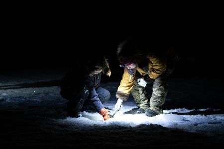 Iriqtaq Hailstone and her sister, Carol Hailstone ice fish in the night. (BBC Studios Reality Productions, LLC/Dwayne Fowler)