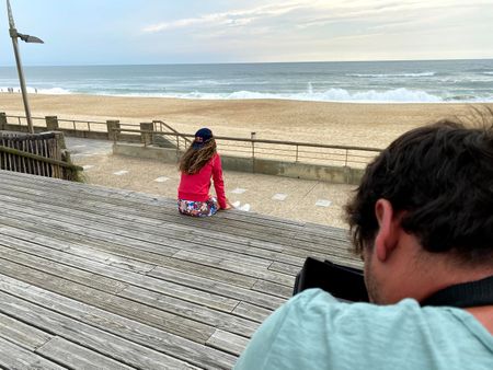 Big wave surfer Justine Dupont sits on steps on the boardwalk next to the beach. DP Alfredo de Juan films from behind.  (National Geographic/Gene Gallerano)
