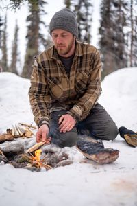 Johnny Rolfe adds kindling to a fire while he builds a box seat for his dog, Java. (BBC Studios Reality Production/Patrick Henderson)