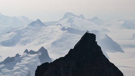 Aerial view of Tommy Caldwell and Alex Honnold celebrating on the summit of the East Cat's Ear Spire, silhouetted against mountains in the background.  (National Geographic/Pablo Durana)