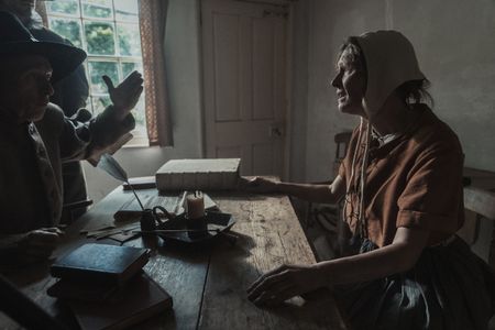 Sarah Good sits at a table, being interrogated for witchcraft. (Dash Productions Services LTD/Antoan Ivanov)