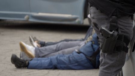 An HSI agent stands with their gun in their holster next to multiple suspects sitting on the ground after being arrested in San Diego, Calif. (National Geographic)