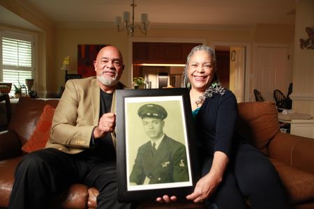Frank Bland and his wife Irene Bland hold a portrait of Frank's father, George Bland, at their home in Richmond Virginia. "Erased: WW2's Heroes of Color" tells the stories of three Black heroes who miraculously survived the attack on Pearl Harbor. One of these men is George Bland, who served as mess attendant on the USS West Virginia. (National Geographic/Nelson Adeosun)