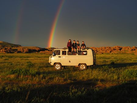 Mia, Leo, Colin, and Laurent Pelletier pose on top of their camper van in front of a double rainbow while in Mongolia. (Credit: Edith Lemay)