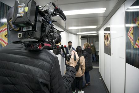 A CBP officer is questioning two travelers in a boarding hall, as a cameraman films on. (National Geographic)