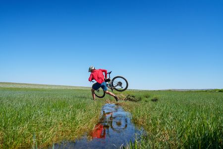 Alex Honnold jumping over a stream with his bike in marshland.(National Geographic/Taylor Shaffer)