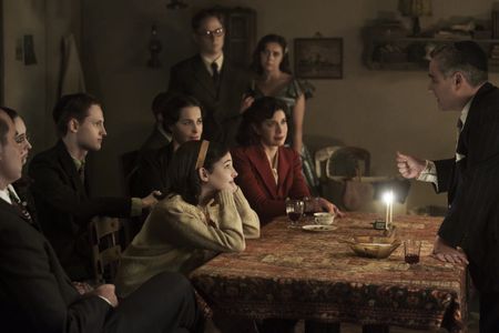 A SMALL LIGHT - Jan and Miep Gies (Joe Cole and Bel Powley) join the Franks and the van Pels (from left: Liev Schreiber as Otto Frank, Ashley Brooke as Margot Frank, Rudi Goodman as Peter van Pels, Amira Casar as Edith Frank, Billie Boullet as Anne Frank and Caroline Catz as Mrs. van Pels) and watch as Mr. van Pels (Andy Nyman) lights the menorah during Hanukkah, as seen the upcoming limited series A SMALL LIGHT, from National Geographic and ABC Signature in partnership with Keshet Studios. (Photo credit: National Geographic for Disney/Dusan Martincek)