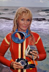 Valerie Taylor in red wetsuit posing with camera equipment.  (photo credit: Ron & Valerie Taylor)