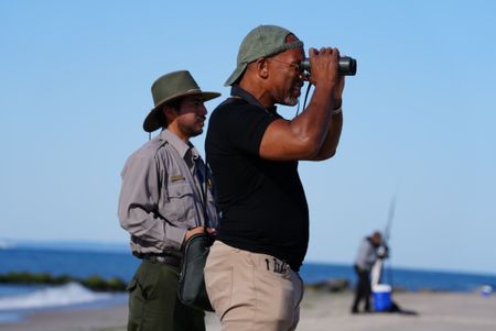 National Park Service biologist Mike Foguer and Christian Cooper watch for a piping plover to return to its nest after setting up an exclosure to protect it.   (National Geographic/Troy Christopher)