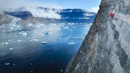 Alex Honnold climbs the lower section of Ingmikortillaq with a glacier in the background.  (photo credit: National Geographic/Pablo Durana)