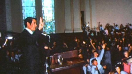 Jim Jones makes a peace sign for his congregation from the pulpit in California. (Don Como)