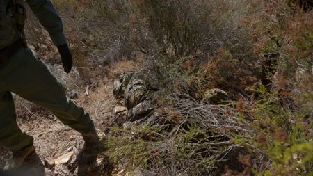 A migrant that was attempting to cross the border illegally is hiding from Border Patrol in camouflage in San Diego, Calif. (National Geographic)