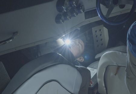 A CBP Agent lies on the ground while holding a flashlight in his mouth to inspect the engine of a boat or water vessel in St Thomas, USVI. (Lucky 8 TV/Paul Taggart)