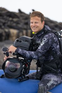 Bertie Gregory in dive gear with an underwater camera sitting on the edge of a small rib preparing to dive. (credit: National Geographic/Zubin Sarosh)