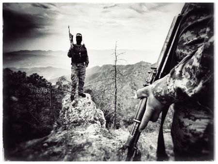A masked narco stands atop rock with vista in Sinaloa mountains. (Nick Quested)