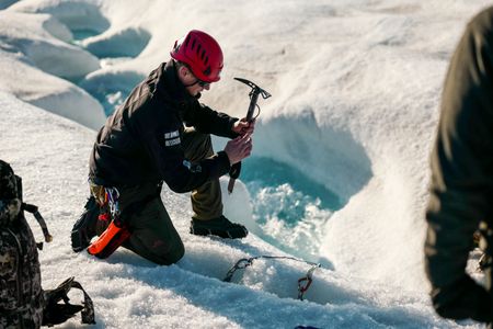 PolarX guide Tom Lawton digs with and ice pick to secure rope for glacier stream crossing. (National Geographic/Mario Tadinac)