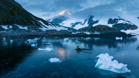 Ralph Bower sits alone on a small rock in the middle of the bay filming Gentoo penguins.  (credit: National Geographic/Bertie Gregory)