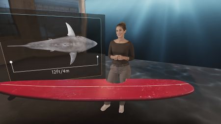 Dr. Diva Amon in the shark studio lab while analyzing a GFX version of Elinor Dempsey's, contributor, shark bitten surfboard whilst a GFX 12ft Great White Shark is displayed in the background. (National Geographic)