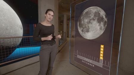 Dr. Diva Amon in the shark lab studio while standing next to GFX 'Coral' information board which is displaying an image of the moon and the increase in shark attacks depending on the lunar cycle. (National Geographic)