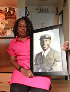 Claudette Simmons holds a portrait of her father, Clark Simmons, in her home in New York. "Erased: WW2's Heroes of Color" tells the stories of three Black heroes who miraculously survived the attack on Pearl Harbor. One of these men was Clark Simmons, who served as mess attendant on the USS Utah. (National Geographic/Nelson Adeosun)