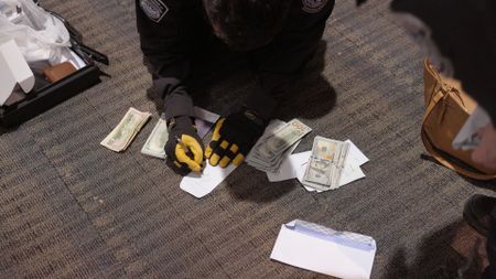 CBP Officer Hundal writes down the amount after counting multiple stacks of currency discovered in a passenger's belongings   in Dulles, Va. (National Geographic)