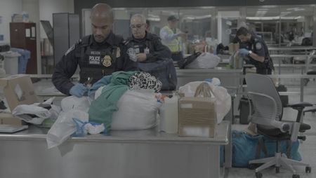 CBP Officer Wilson inspects a package found in a courier's belongings in Dulles, Va. Fellow officers Hundal and Augustino perform other inspetions in the background. (National Geographic)