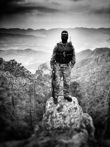 A masked narco stands atop rock with vista in Sinaloa mountains. (Nick Quested)
