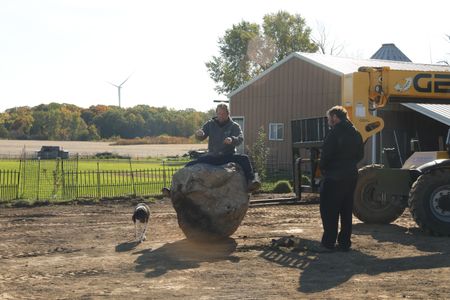 Dax, Ben's dog, walks by Ben Reinhold sitting on and pretending to drive the new garden's centerpiece rock while Charles Pol watches. (National Geographic)