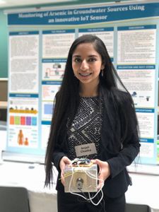 Anjali in front of her science fair project board. Holding arsenic detector.  (National Geographic)