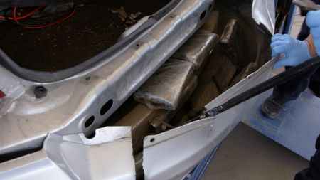 Two CBP officers use crowbars to access hidden packages of suspected narcotics from the rear bumper of a suspect's vehicle in El Paso, Texas. (National Geographic)