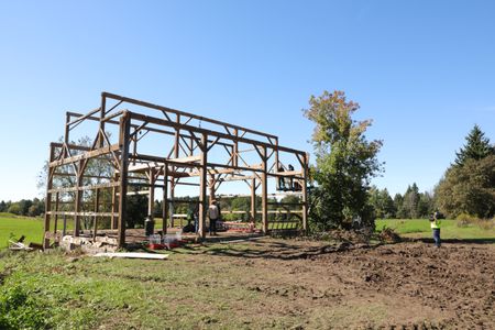 Ben Reinhold and Charles Pol on a lift plan out how to take down the beams from the old barn they want to transport and restore on the Pol family's farmland, as others watch and a crew member films them. (National Geographic)
