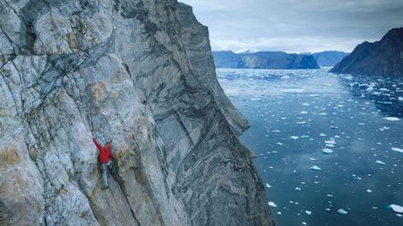 Alex Honnold climbs with mountains and water in the background.  (photo credit: National Geographic/Pablo Durana)