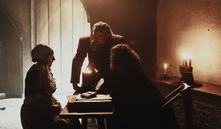 John Stearne stands over his partner, Matthew Hopkins, as the pair interrogate a suspected witch inside a dim lit room. (Dash Productions Services LTD/Antoan Ivanov)