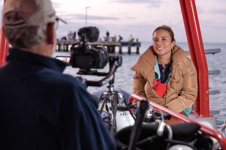 Cinematographer Rory McGuinness filming an interview with Dr. Alex Schnell aboard a dive vessel in Port Philip Bay. Alex hugs a water bottle to keep warm in the frigid temperatures.   (National Geographic for Disney/Harriet Spark)