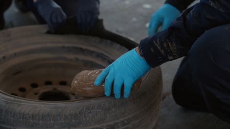 CBP Officer Gonzalez holds a package of suspected narcotics after extracting it from the tire of a suspect's vehicle. in Miami, Fla. (National Geographic)